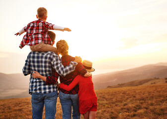 Happy family: mother, father, children son and daughter  backs are turned on sunset