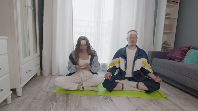 Young fit family sitting on the floor, meditating together, keeping a healthy lifestyle. Woman take photo on her boyfriend
