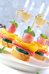 Tasty canapes with cucumber, salami, cheese and grapes served with white wine. Top view with copy space.