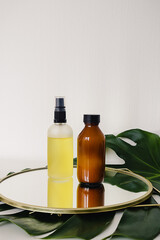 Various amber and matte glass bottles for cosmetics, natural medicine , essential oils or other liquid on a white background standing on a mirror decorated with a green monstera leaf