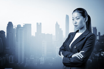 Fototapeta na wymiar Prosperous Asian businesswoman in suit in crossed arms pose. Bangkok cityscape. The concept of woman in business. Financial downtown. Double exposure.