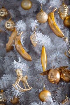 Golden christmas toys hanging on white artificial christmas tree