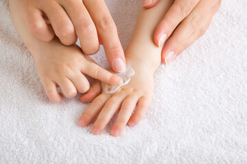 Obraz na płótnie Canvas Young mother and baby fingers together applying moisturizing cream on baby hand on white towel. Care about children clean and soft body skin. Front view. Closeup.