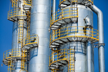 Close-up of grey metal oil refining columns (distillation towers) on blue sky. Oil refinery and gas processing plant.