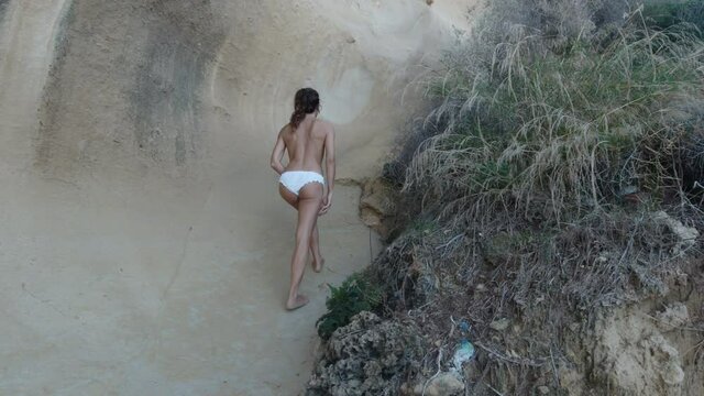 woman bare foot and topless walking along the rock coast and sand on the beach. Travel Concept.