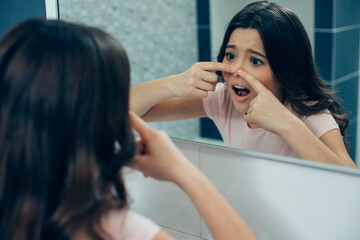 Expressive teenager looking at her nose in the mirror