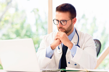 Male doctor sitting at desk and using laptop while working in doctor's office