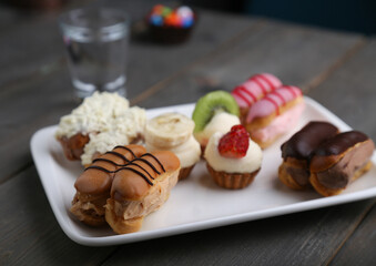 Eclairs and mini tarts on a white plate with a glass of water