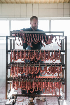 Young butcher adding row of fresh sausages to smoking rack
