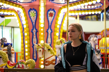 Fototapeta premium Beautiful stylish girl stands near the carousel in the amusement park