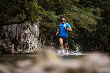 Fototapeta premium Young man in sports equipment running in mountain river