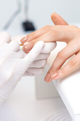 Manicure master in protective gloves applying beige nail polish on female nails in beauty salon