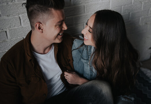Young couple together hugging and laughing against white brick wall