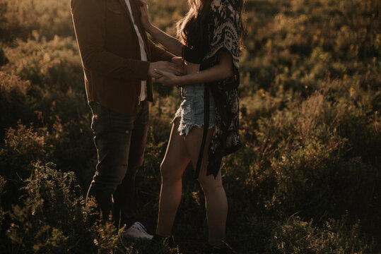 Young attractive fashionable couple holding hands in field at sunset