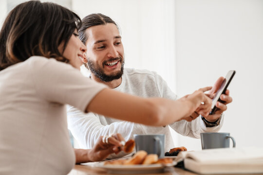 Image of smiling couple using mobile phone while having breakfast