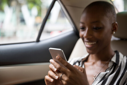 Portrait of a young African American woman sitting n backseat of car looking at cell phone