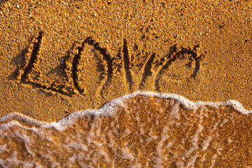 The word love is written on the sandy seashore.