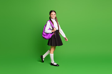 Photo portrait of young girl walking with violet school bag on one shoulder isolated on vivid green colored background - Powered by Adobe