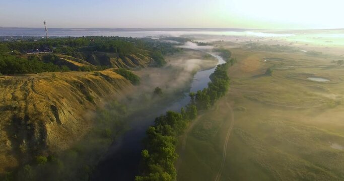 Aerial view of pink sunrise on misty valley of Siverskyi Donets river near Zmiiv city, Ukraine. Lifting camera over riverbed overlooking the city