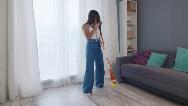 Young positive caucasian woman funnily dancing while cleaning the house