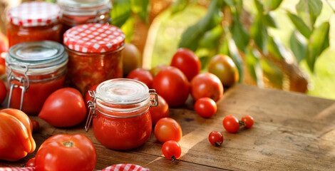 Homemade tomato preserves in a glass jars and fresh tomatoes  on a wooden table close up view