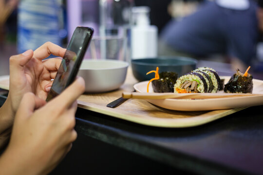 Korean food market snack concept with a marinated beef kimbap plated on bambu with chopsticks and bokeh background for negative space and a smartphone taking photos for social media business.
