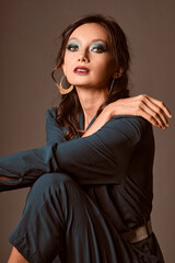 Naklejka premium Portrait of a sexy brunette woman seated in a black stool wearing a green dress and looking at camera over a grey background