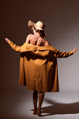 Sexy brunette young woman portrait showing her back and shoulders wearing a yellow coat with a hat