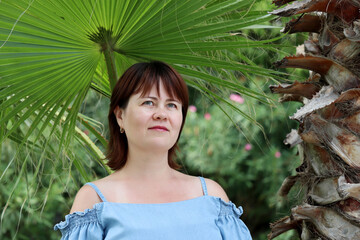 Tropical vacation, happy middle age woman dreaming on a beach on palm tree background. Concept of enjoying of romantic leisure and relax on a paradise nature