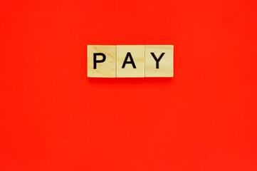 Word pay. Wooden blocks with lettering on top of red background. Top view of wooden blocks with letters on red surface