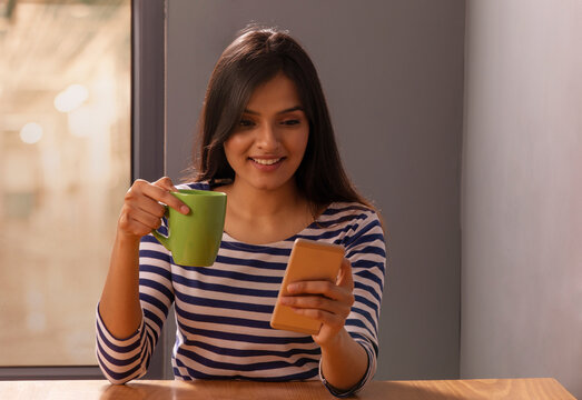 Woman looking at her phone with a coffee mug in her hand	