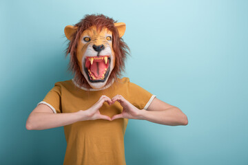 Young woman in lion mask shows love heart affection hand gesture, isolated on blue background