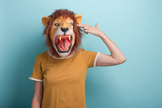 Young woman in lion mask pointing fingers to head in gun hand gesture imitating suicide, isolated on blue background.