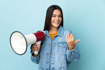Teenager girl isolated on yellow background holding a megaphone and inviting to come with hand
