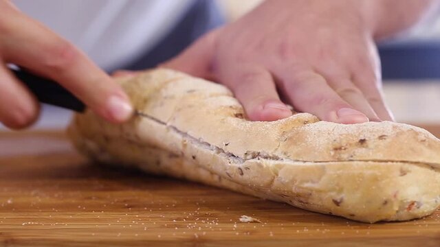 Cooking  delicious sandwich in kitchen at home. man cuts crisp loaf with a sharp knife to prepare sandwich. Morning Breakfast and lunch. Fast street food in  restaurant.