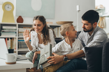 Obraz premium family sharing gifts and having video call on laptop computer, sitting on sofa at home