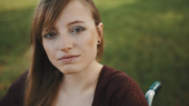 Portrait of beautiful young caucasian paralyzed woman in wheelchair stroking her hair on autumn breeze. High quality 4k footage