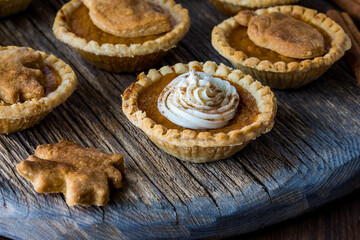 Close up of pumpkin pie tarts garnished with icing and cinnamon sprinkles and pie shell leaf shapes.