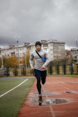 Fototapeta na wymiar An athlete in a gray jacket and black leggings runs on a red treadmill at the stadium. Scamper. Sports as a lifestyle. out of focus