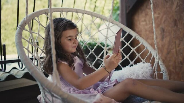 female child having leisure time in swing on home terrace