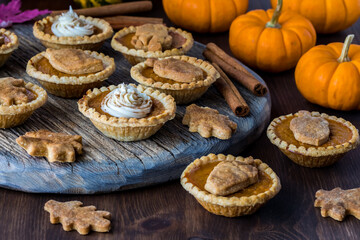 Wooden platter of pumpkin pie tarts surrounded by mini pumpkins. 