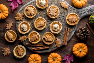Obraz na płótnie Canvas Top down view of various decorated pumpkin pie tarts surrounded by fall decorations.