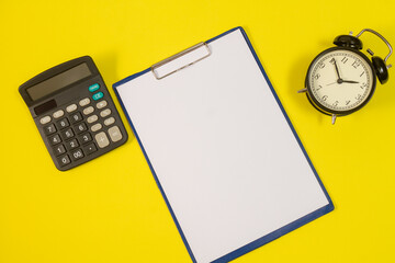 Stationery or essential office tools. Sheets of office paper, calculator and alarm clock on a yellow background, top view.