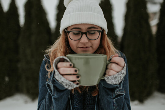Lifestyle photo of a girl drinking from a large mug outdoors in the snow in front of trees in the winter