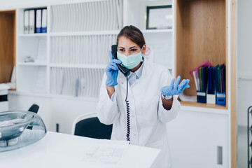 Fototapeta na wymiar Young female practitioner or nurse with face protective mask working at clinic reception desk.