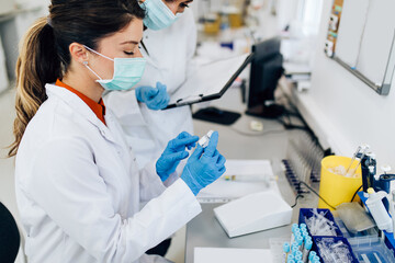 Naklejka premium Two female scientists or technicians with face protective masks work in laboratory on human blood samples.