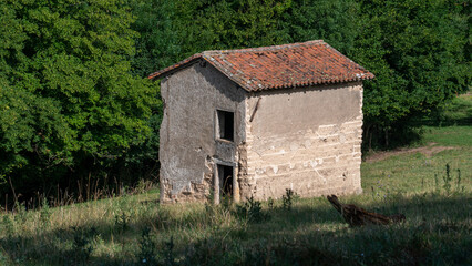 vieille maison inhabitée, vue  dans un pré en pente avec mur en pisé, il y a des arbres en arrière plan