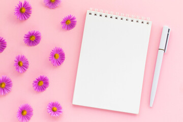 Michaelmas daisy buds and blank notepad with pen on pink background. Notebook for ideas message, list and inspiration. Flat lay, top view with copy space. Mockup for your design. 