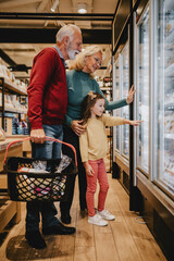 Happy grandmother and grandfather with granddaughter shopping together in grocery store or...