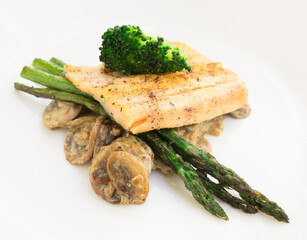 dish of fried river trout fillet with garnish of broccoli, asparagus sprouts and mushroom sauce on white background